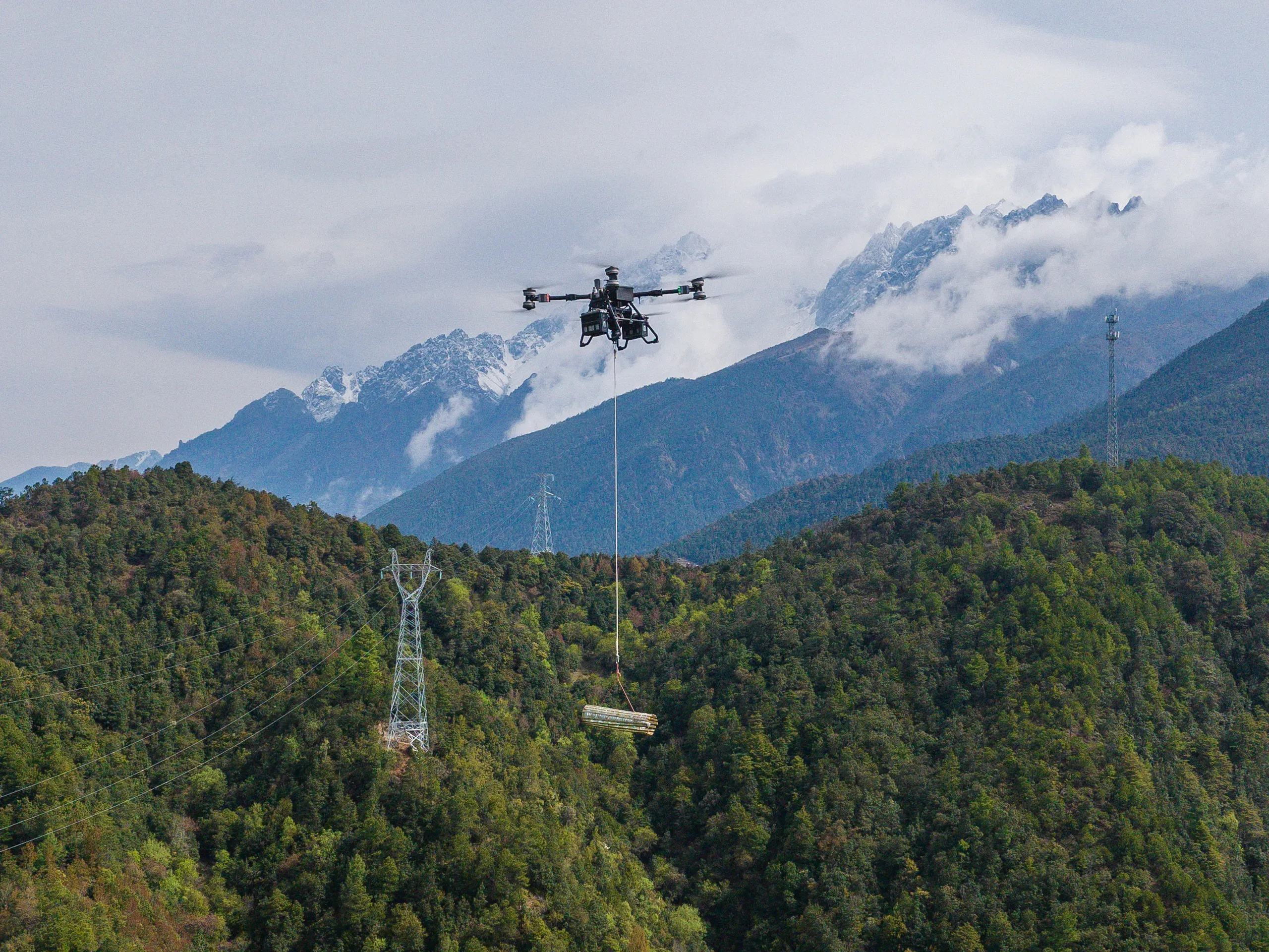 Lastendrohne DJI FlyCart 100 transportiert Material am Windenseil über unwegsames Waldgebiet im Gebirge